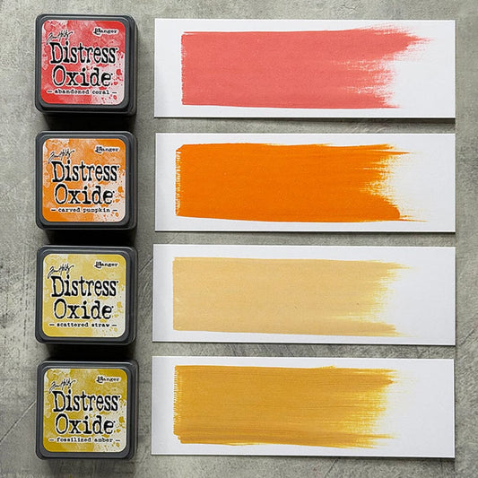 Four Ranger Distress Oxide ink pads from Kit 14 with swatched colours: Abandoned Coral, Carved Pumpkin, Scattered Straw and Fossilized Amber, shown on white paper beside each labelled pad.
