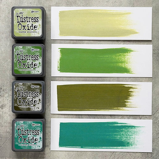 Four Ranger Distress Oxide ink pads from Kit 15 with swatched colours: Shabby Shutters, Mowed Lawn, Forest Moss and Lucky Clover, shown on white paper beside each labelled pad.
