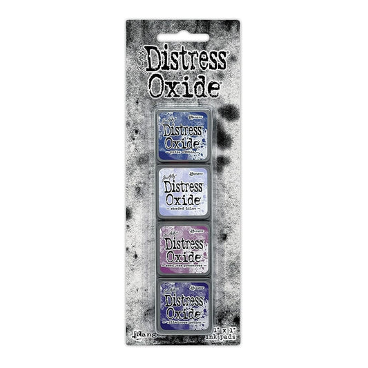 Packaged set of four Ranger Distress Oxide Mini Ink Pads from Kit 5 in Prize Ribbon, Shaded Lilac, Seedless Preserves and Villainous Potion, shown in original Tim Holtz packaging with grungy black-and-white background.
