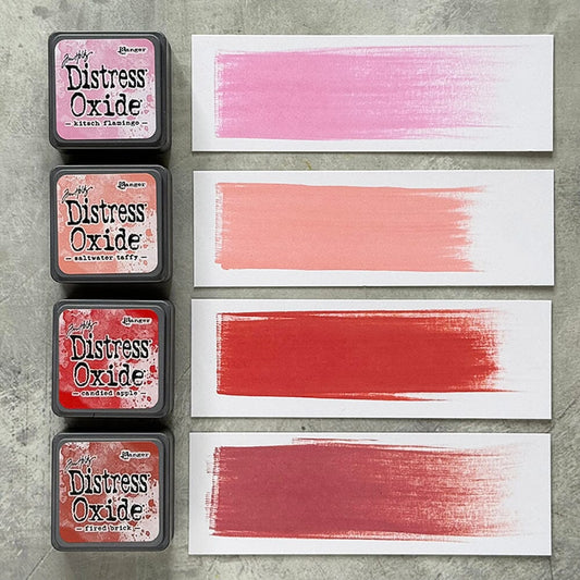 Four Ranger Distress Oxide ink pads from Kit 7 with swatched colours: Kitsch Flamingo, Saltwater Taffy, Candied Apple and Fired Brick, shown on white paper beside each labelled pad.
