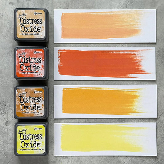 Four Ranger Distress Oxide ink pads from Kit 8 with swatched colours: Dried Marigold, Ripe Persimmon, Wild Honey and Squeezed Lemonade, shown on white paper beside each labelled pad.
