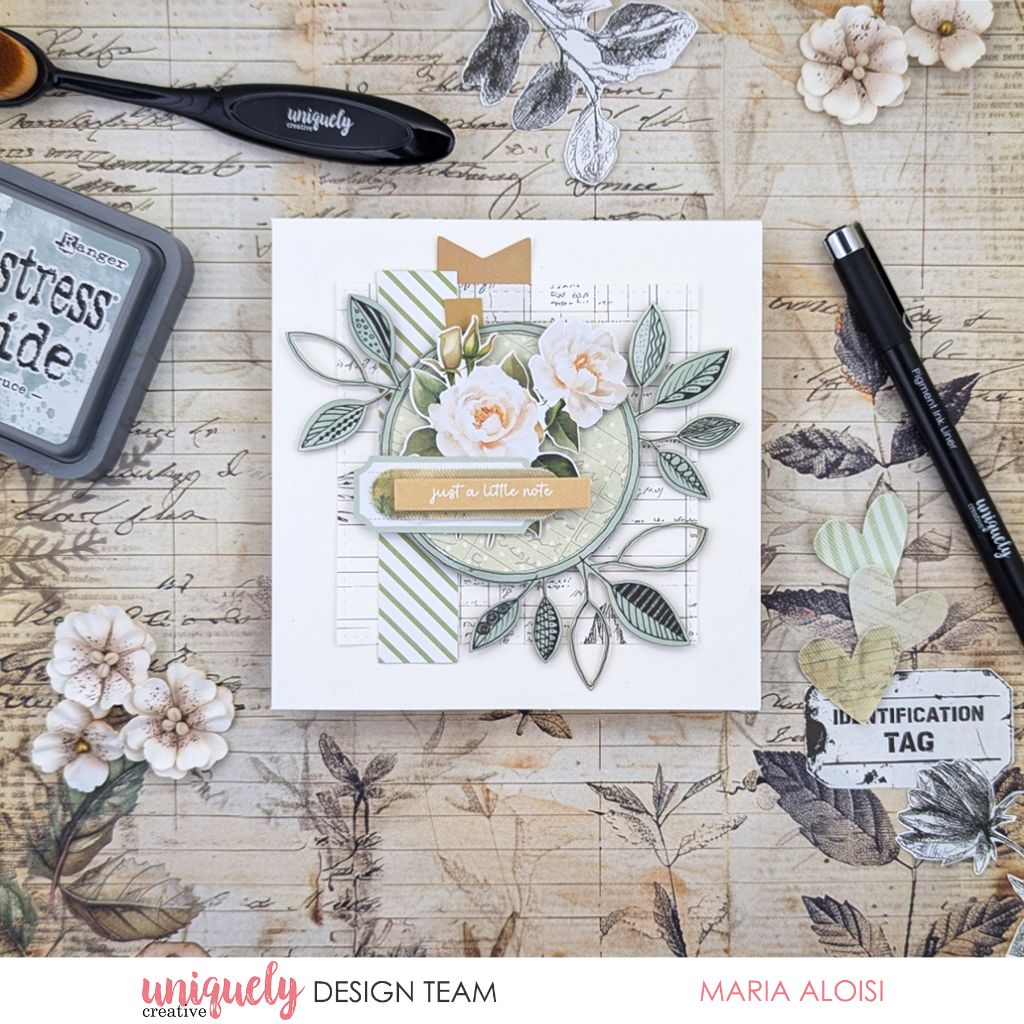 Handmade card by Maria Aloisi using Uniquely Creative Botanical Chronicles collection – features layered florals and leaves on a vintage botanical background with the sentiment “just a little note.” Surrounded by crafting tools and paper cutouts, the design blends elegance with a warm, personal touch.
