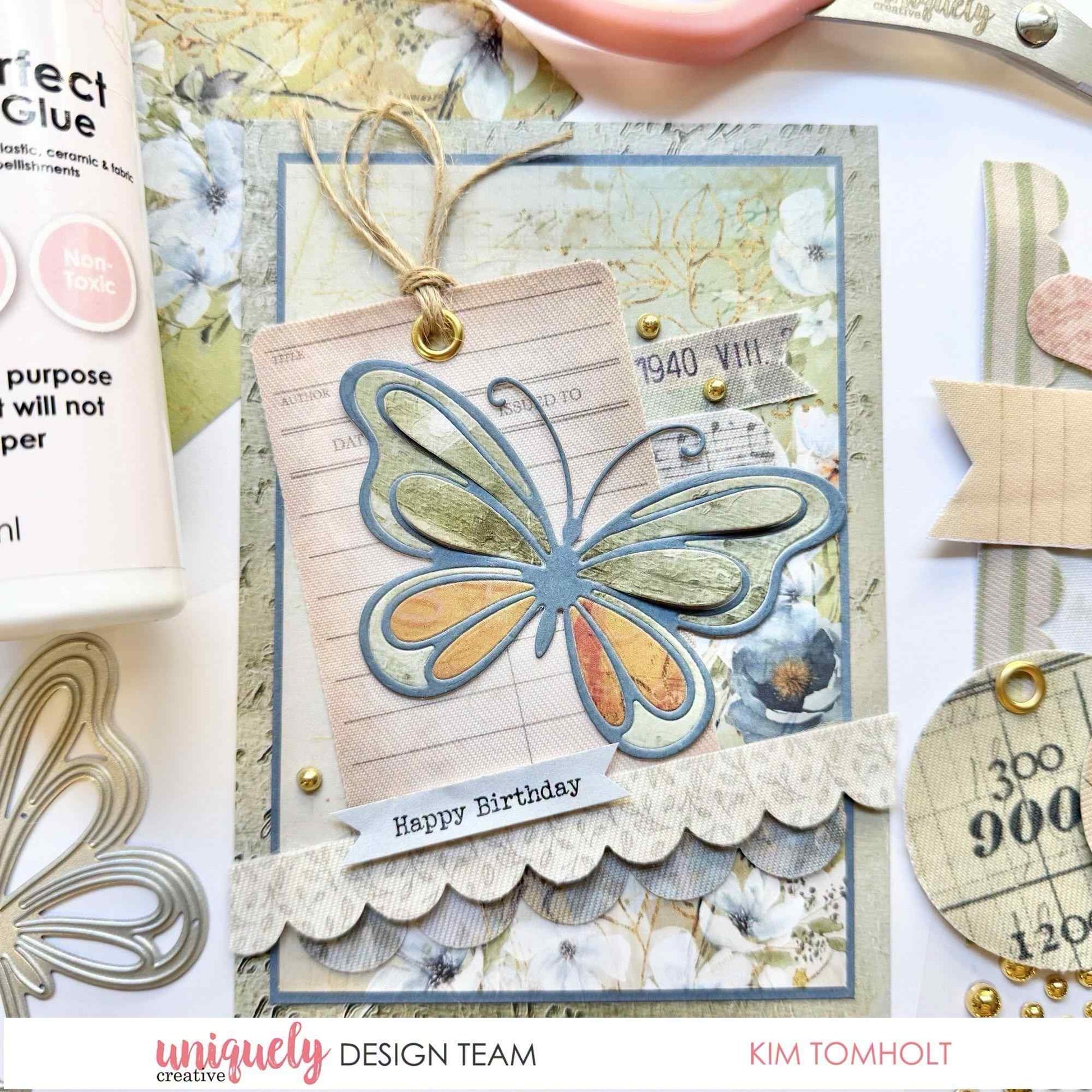 Handmade birthday card sample using the Uniquely Creative Delicate Butterfly Die, featuring a layered blue butterfly die-cut over a vintage library card tag on soft floral patterned paper with a "Happy Birthday" sentiment 