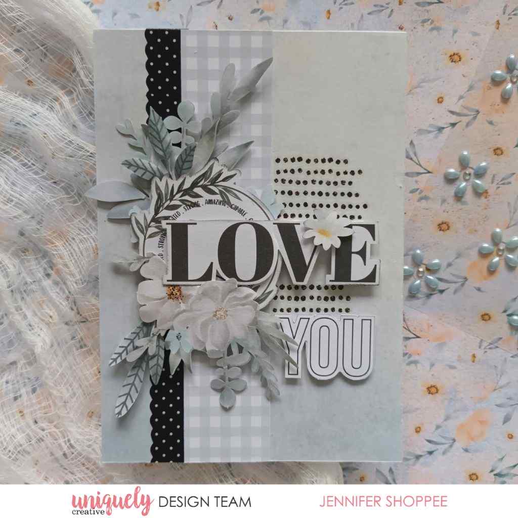 Handmade card sample with “LOVE YOU” lettering, white floral embellishments, pale gingham paper and black polka-dot layers.