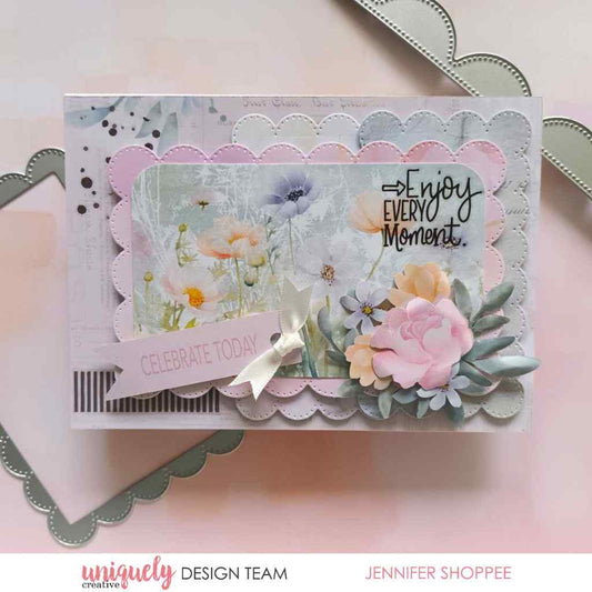Handmade card sample featuring a floral paper panel, layered scalloped borders, a white bow, floral embellishments and “Enjoy Every Moment” lettering.⠋
