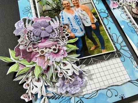 Scrapbook layout of two women in a garden, decorated with layered flowers, butterflies and a lace doily accent