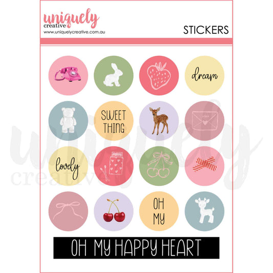 Uniquely Creative Oh So Lovely Little Happy Things Chipboard Stickers sheet showing 16 circular 1 inch stickers with illustrated designs including a pink telephone, bunny, fawn, cherries, strawberry and sentiments Dream, Sweet Thing, Lovely and Oh My on soft pastel backgrounds