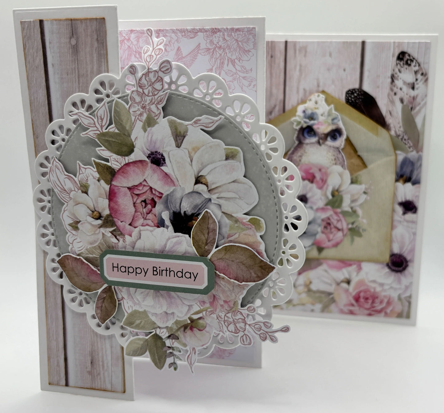 Handmade tri-fold card using Uniquely Creative Delicate Doily Die with white doily frame, pink and white florals, sage leaves and Happy Birthday sentiment on grey woodgrain background 