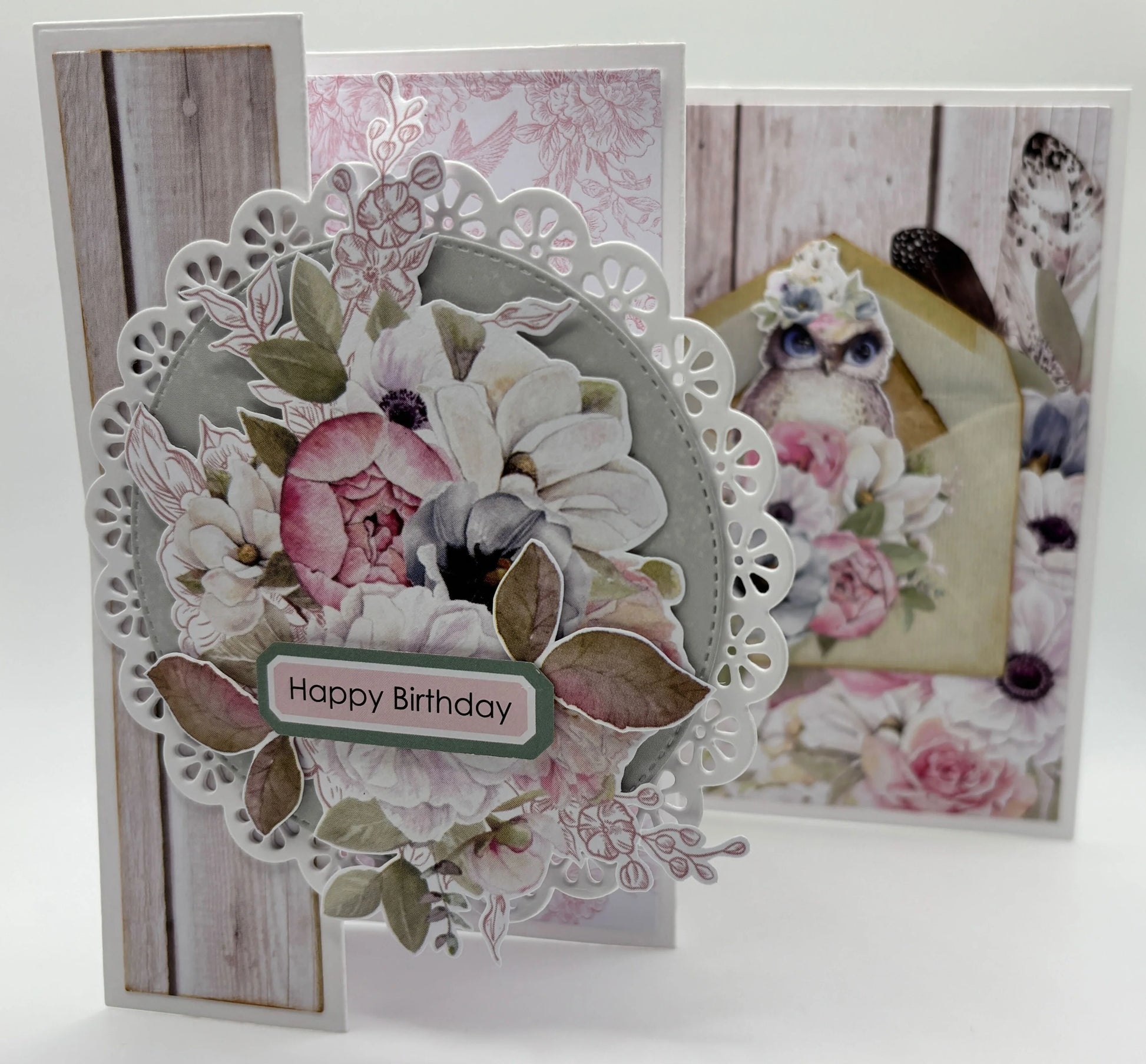 Handmade tri-fold card using Uniquely Creative Delicate Doily Die with white doily frame, pink and white florals, sage leaves and Happy Birthday sentiment on grey woodgrain background 