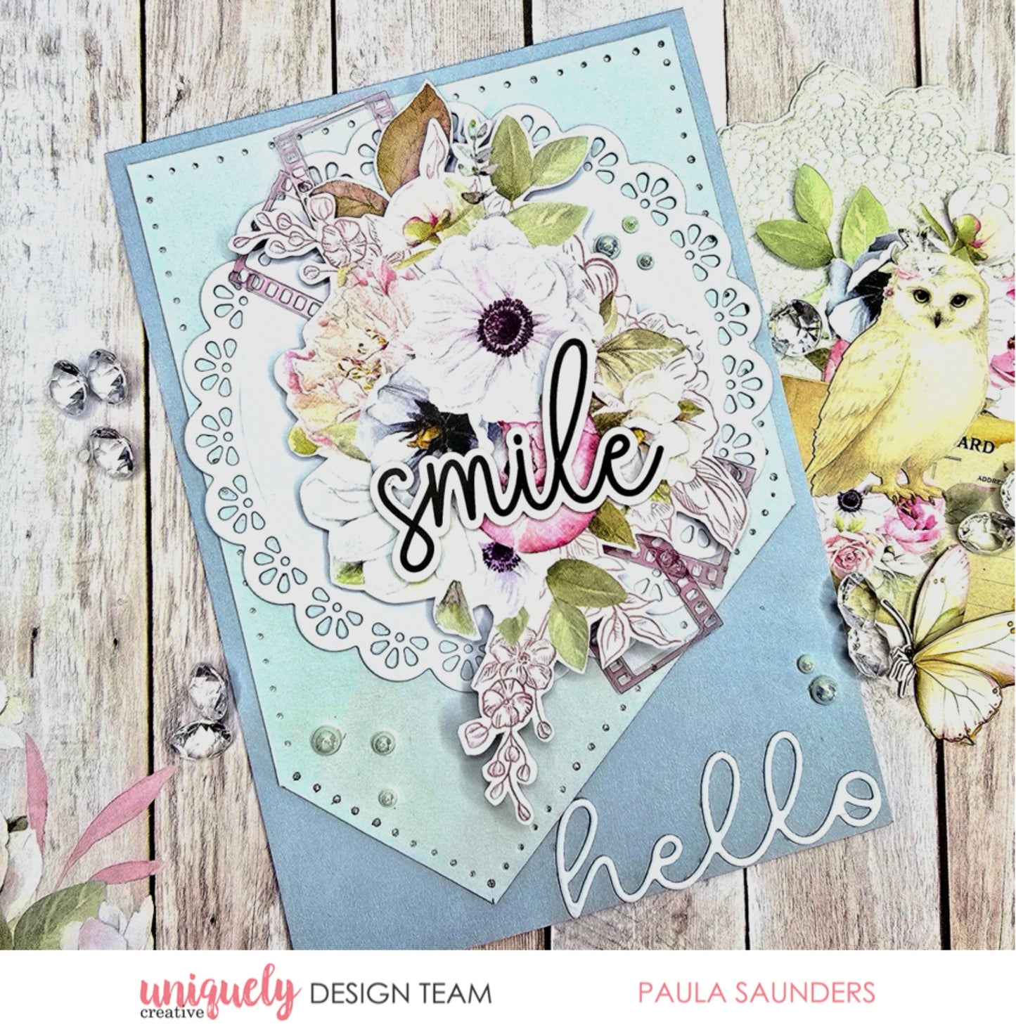 Handmade greeting card using Whispers of Wisdom papers featuring white anemone florals, smile sentiment die cut, decorative doily, and butterfly embellishments on light blue cardstock with pearl accents
