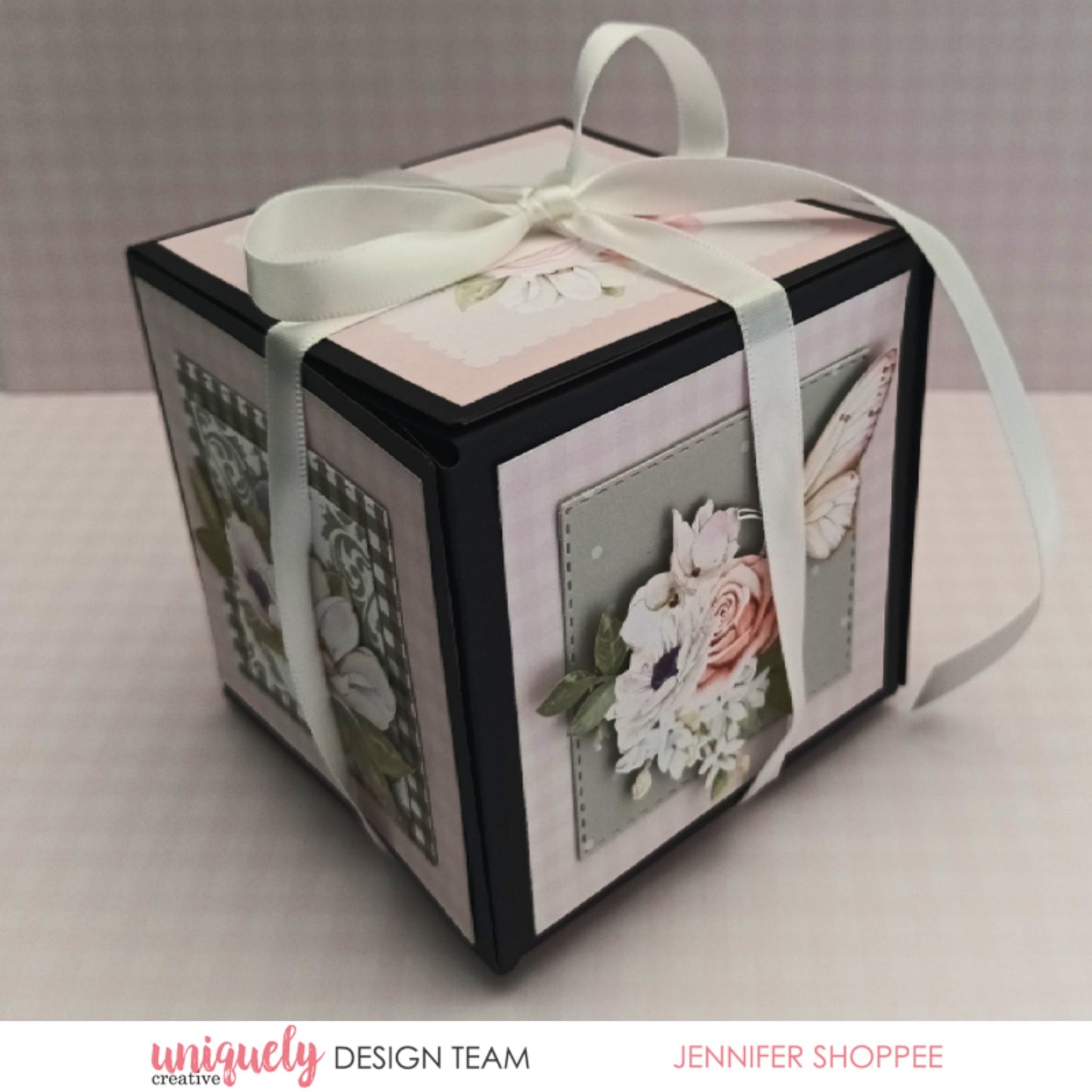 Assembled memory box folio decorated with floral papers, embellishments and white ribbon, demonstrating finished 3D cube design