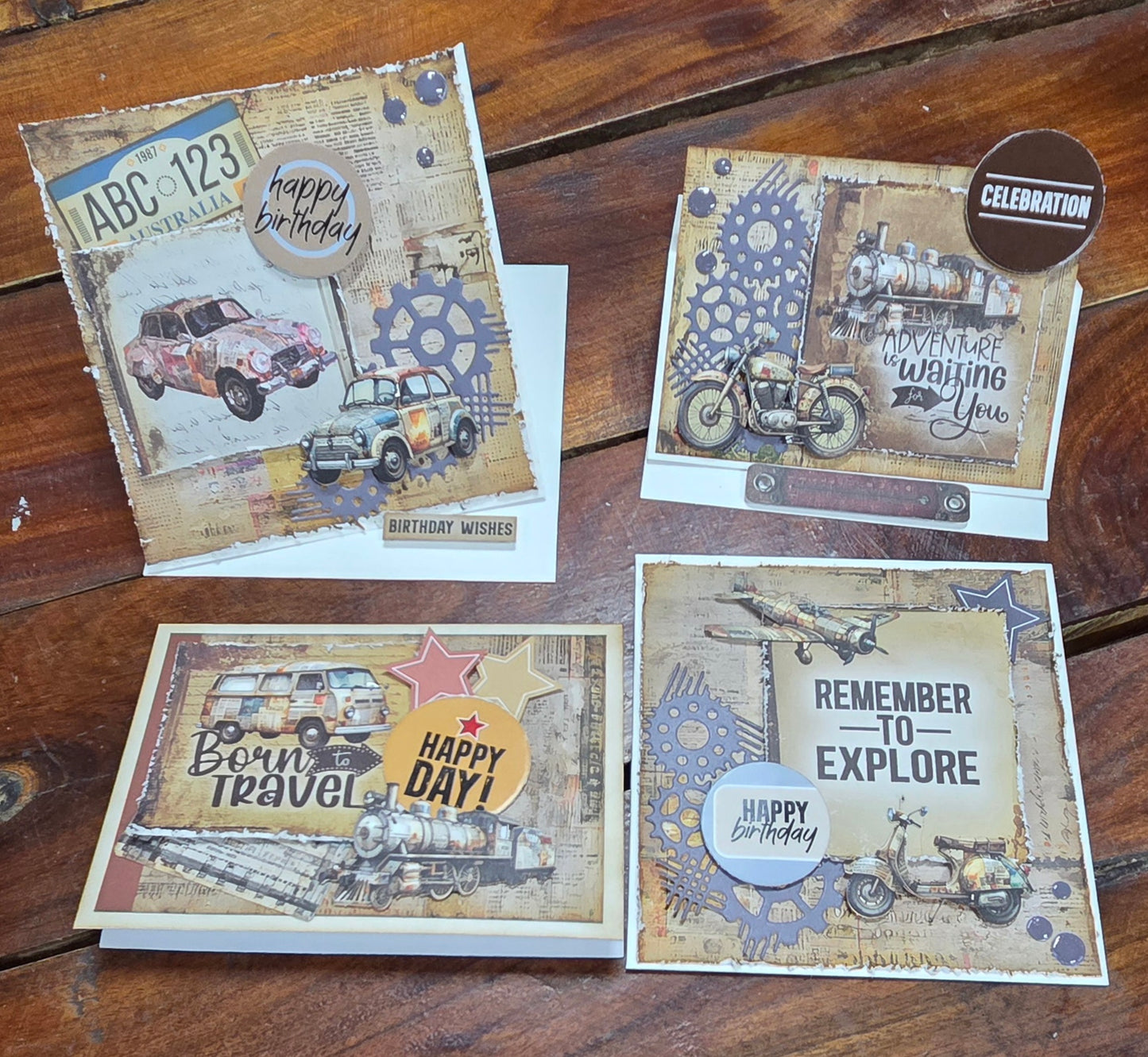 Four handmade birthday cards using Wings and Wheels papers featuring vintage cars, motorcycles and trains in masculine earthy tones, displayed on a timber surface
