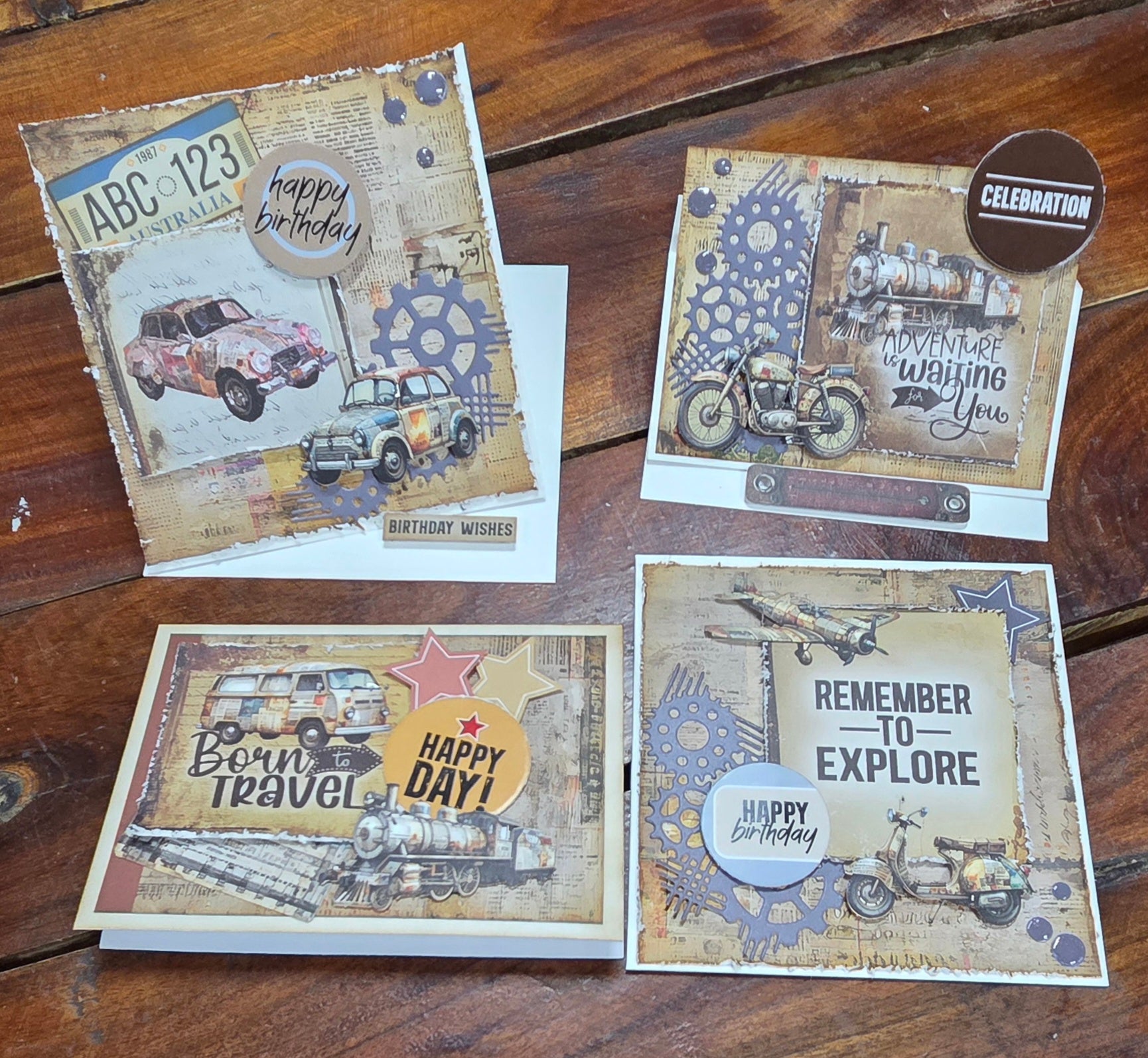 Four handmade birthday cards using Wings and Wheels papers featuring vintage cars, motorcycles and trains in masculine earthy tones, displayed on a timber surface